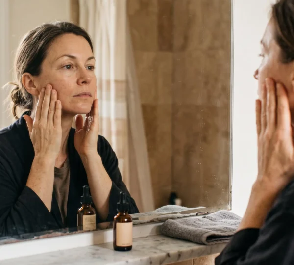 Une femme réalise un auto-massage lifting du visage devant son miroir de salle de bain le matin.